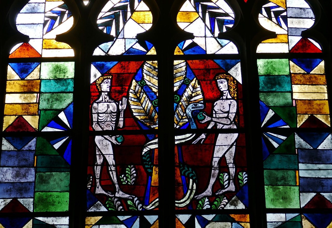 image of dark blue and black stained glass window depicting adam and eve in the garden of eden
