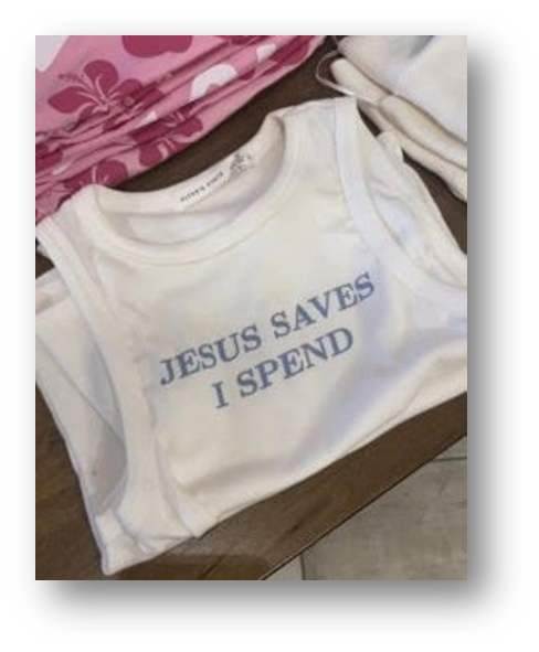 White t-shirt with words "Jesus Saves, I Spend" in blue, folded on a table from the store Altar'd State